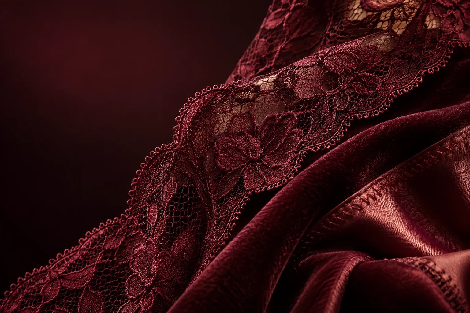 Editorial close detail of burgundy lace and satin textures; atmosphere, not exact product photography.